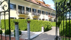 Un bâtiment à la façade jaune, doté de nombreux balcons et agrémenté d’un jardin bien entretenu, avec des haies et des piliers en pierre.