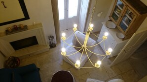 Ein Kronleuchter mit mehreren Lampen, ein Kamin, ein blauer Sessel und eine Holzkabine mit Glastüren.