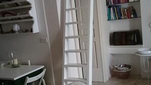 Ein Zimmer mit einem weißen Sofa, einer Wendeltreppe zu einer Schlafgalerie, einem Bücherregal und einem kleinen Tisch mit Stühlen.