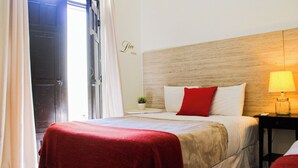 A hotel room with a bed, a nightstand with a lamp, a small potted plant, and a wall sign that reads "Live Well".