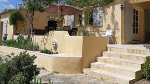 Ein zweistöckiges Gebäude mit einer beige farbenen Fassade, einer überdachten Terrasse und einer Treppe aus Beton, die zum Eingang führt.
