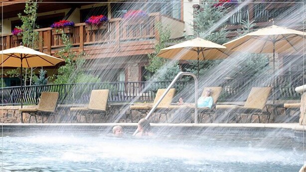 A pool area with lounge chairs and umbrellas, a waterfall feature, and a stone wall.