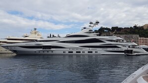 Un grand yacht à plusieurs ponts était amarré dans une marina, avec une vue sur la ville en arrière-plan.