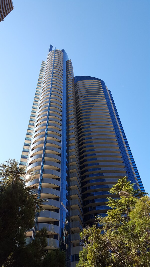 A tall, modern skyscraper with a curved design, featuring multiple balconies and a glass facade.