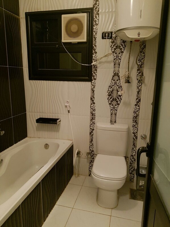 Une salle de bain avec une baignoire, des toilettes et une fenêtre équipée d’un ventilateur.