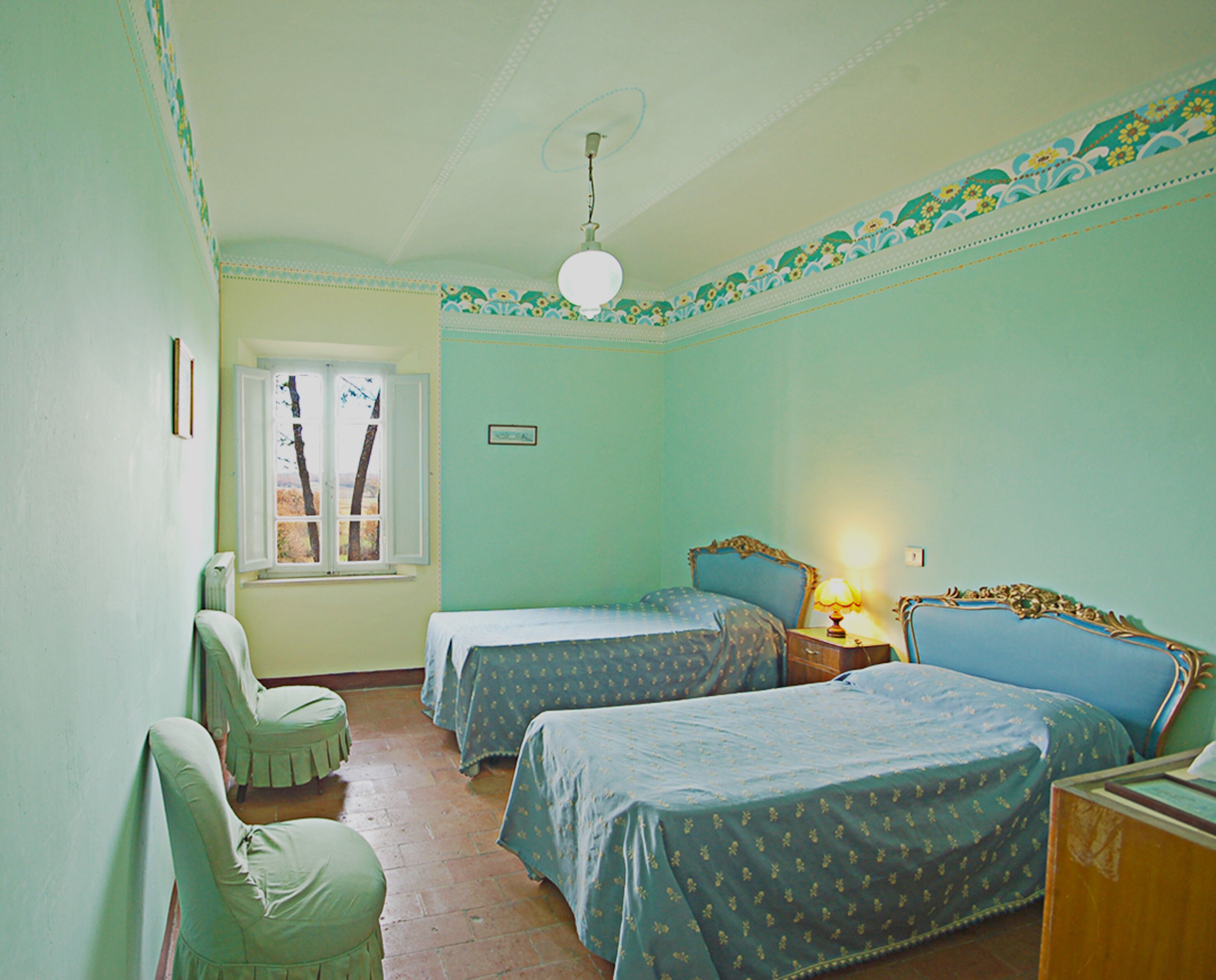 Una habitación con dos camas, una silla, una ventana y un ventilador de techo.