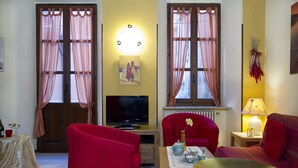 Un salon avec un téléviseur, des fauteuils rouges, une table avec un vase et une lampe.