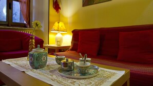 Une pièce avec une table mise pour le thé, un canapé rouge et une fenêtre avec des rideaux.
