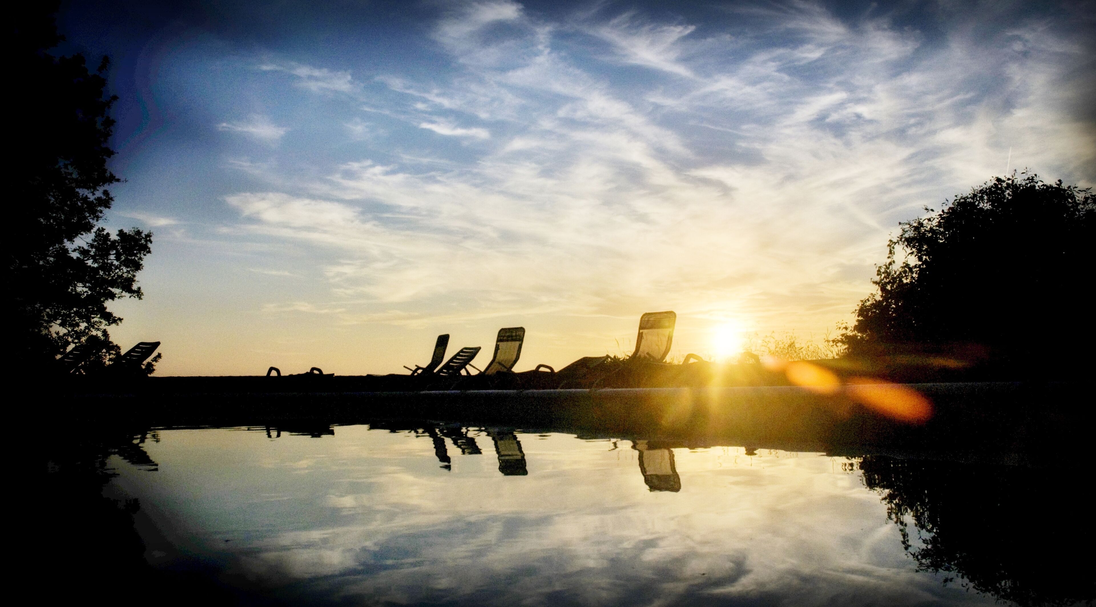 Un atardecer sobre aguas tranquilas, con sillones de descanso y un edificio a lo lejos.