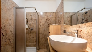 Un baño moderno con ducha de vidrio, un lavamanos ovalado grande y un tocador de madera.