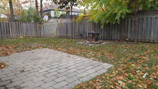 Un patio trasero con zona de terraza empedrada, cerca de madera y antena parabólica.