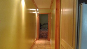 Un pasillo estrecho con paredes amarillas, un marco de puerta de madera y una cama al fondo.