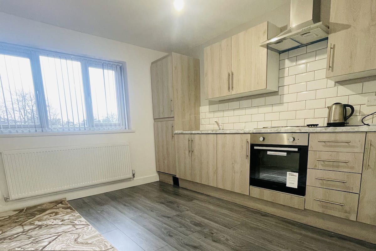 A modern kitchen with light wood cabinets, a built-in oven, and a window with blinds.