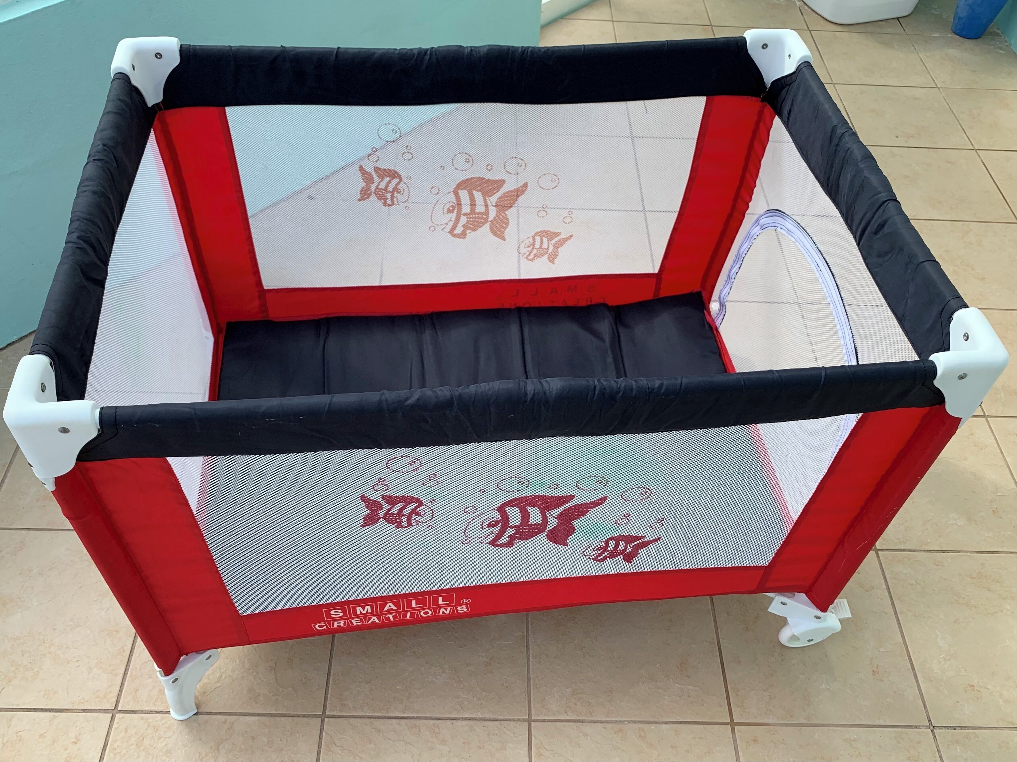 Ein rotes und schwarzes Baby-Spielgehege mit einem Netzoberteil und einem festen Boden, mit dem Schriftzug „SMALL CREATIONS.