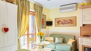 Una habitación acogedora con cama, un sofá verde, una mesa de comedor con sillas, una zona de cocina y un amplio ventanal con cortinas.