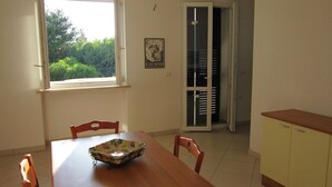 Ein Essbereich mit einem Holztisch, Stühlen, einer Obstschale, einem Fenster und einer Tür, die auf einen Balkon führt.