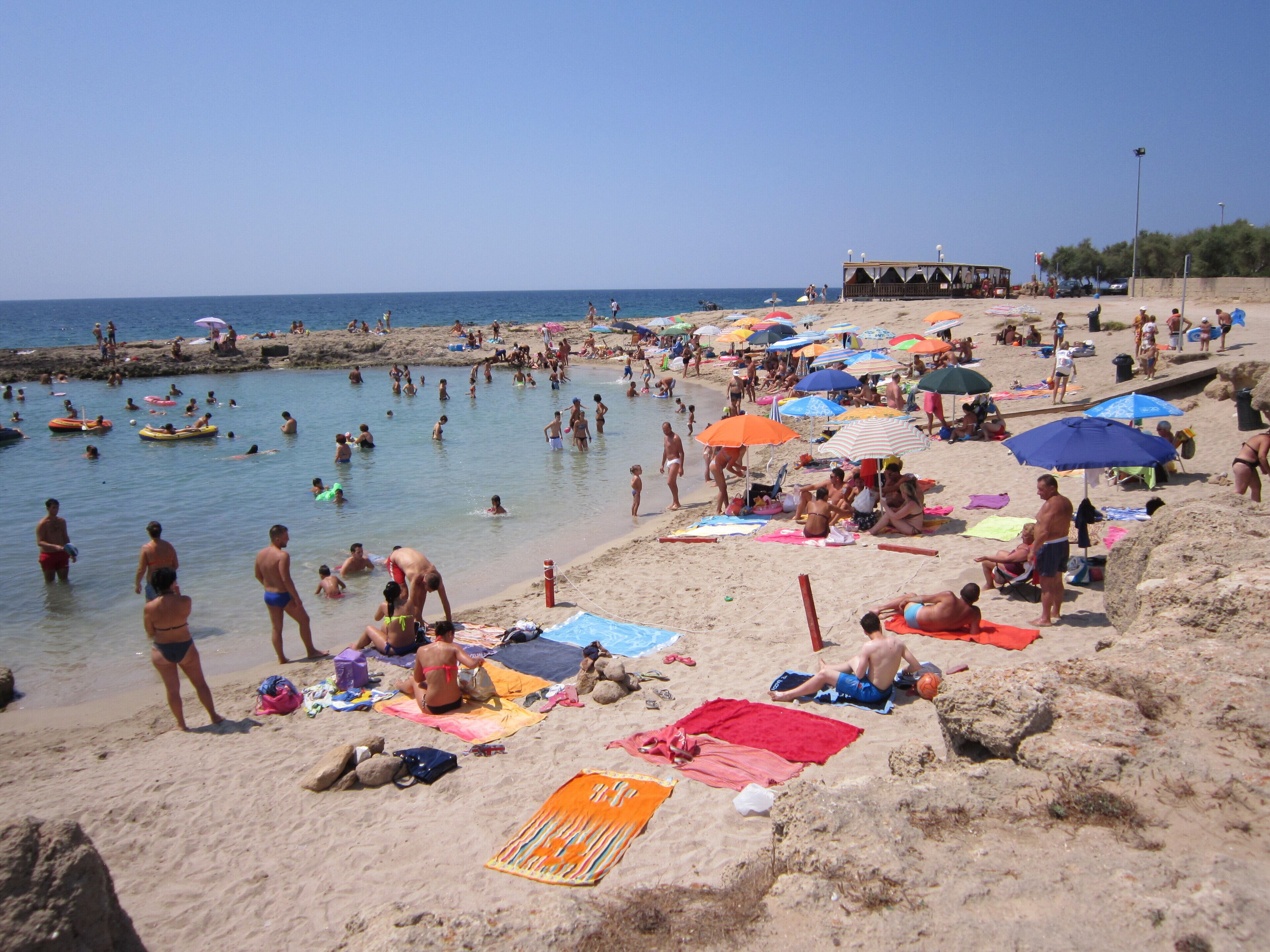 A crowded beach with people sunbathing and swimming.