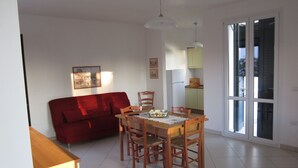 Ein Essbereich mit Holztisch und -stühlen, einem roten Sofa und einer Küche im Hintergrund.