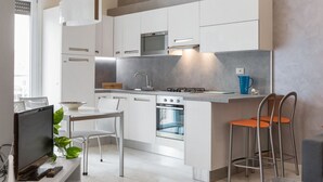 Eine moderne Küche mit weißen Schränken, einem eingebauten Backofen, einem Gasherd und einer Bar mit Sitzgelegenheiten.