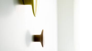 Primer plano de una pared con dos pomos de puerta, uno amarillo y otro marrón, y una puerta blanca al fondo.