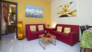 A living room with two red sofas, a wooden coffee table, and a painting of flowers on the wall. - PRETTY CENTRAL APARTMENT, HISTORIC CENTER WITH PARTIAL LAKE VIEW (Orta San Giulio)