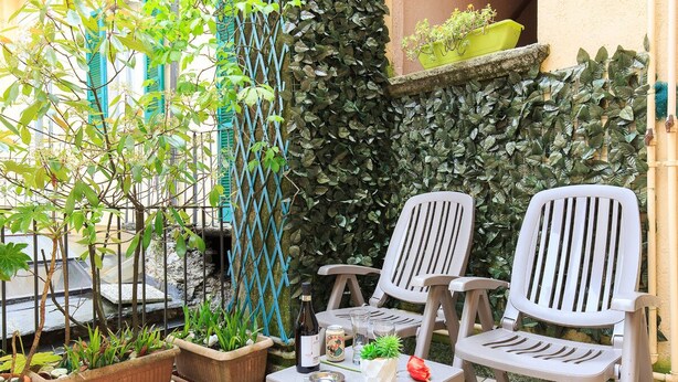 A patio with two white plastic chairs, a small table with a bottle, glasses, and a plate. There are potted plants and a wall covered in ivy. - PRETTY CENTRAL APARTMENT, HISTORIC CENTER WITH PARTIAL LAKE VIEW (Orta San Giulio)