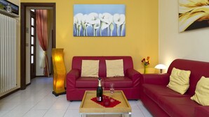 A living room with a red sofa, a wooden coffee table with a bottle and glass, and a painting of white flowers on the wall. - PRETTY CENTRAL APARTMENT, HISTORIC CENTER WITH PARTIAL LAKE VIEW (Orta San Giulio)
