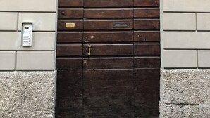 Een donkerhouten deur met een metalen hekwerk, een keypad en een plaquette op een beigekleurde bakstenen muur.