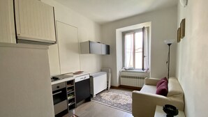 Een compacte leefruimte met kitchenette, een eetgedeelte en een zithoek met een bank en een kleine tafel.