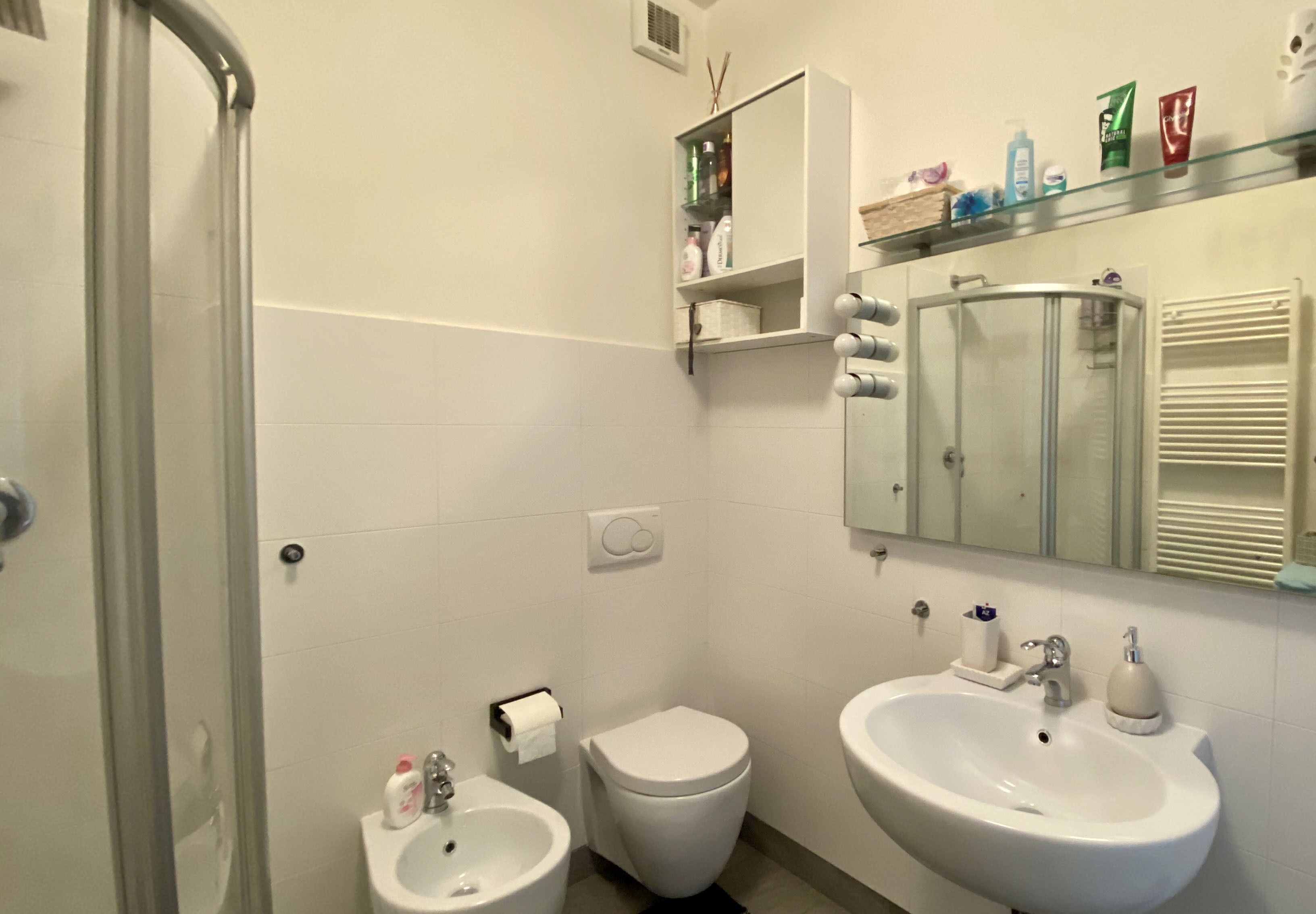 Ein Badezimmer mit Duschkabine, Toilette, Bidet, Waschbecken und Spiegel.