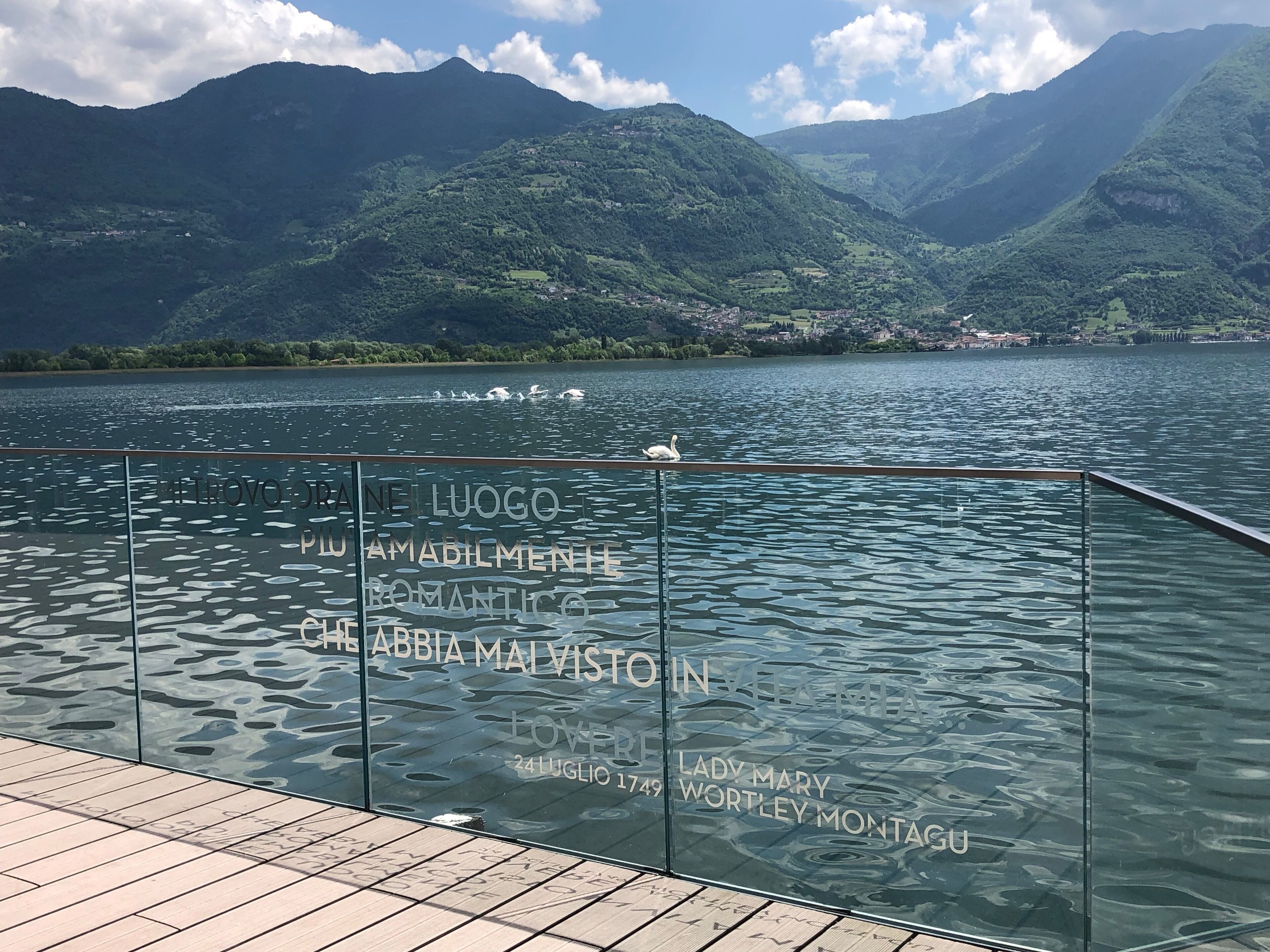 Een glazen balustrade met gegraveerde tekst, een meer en bergen op de achtergrond.