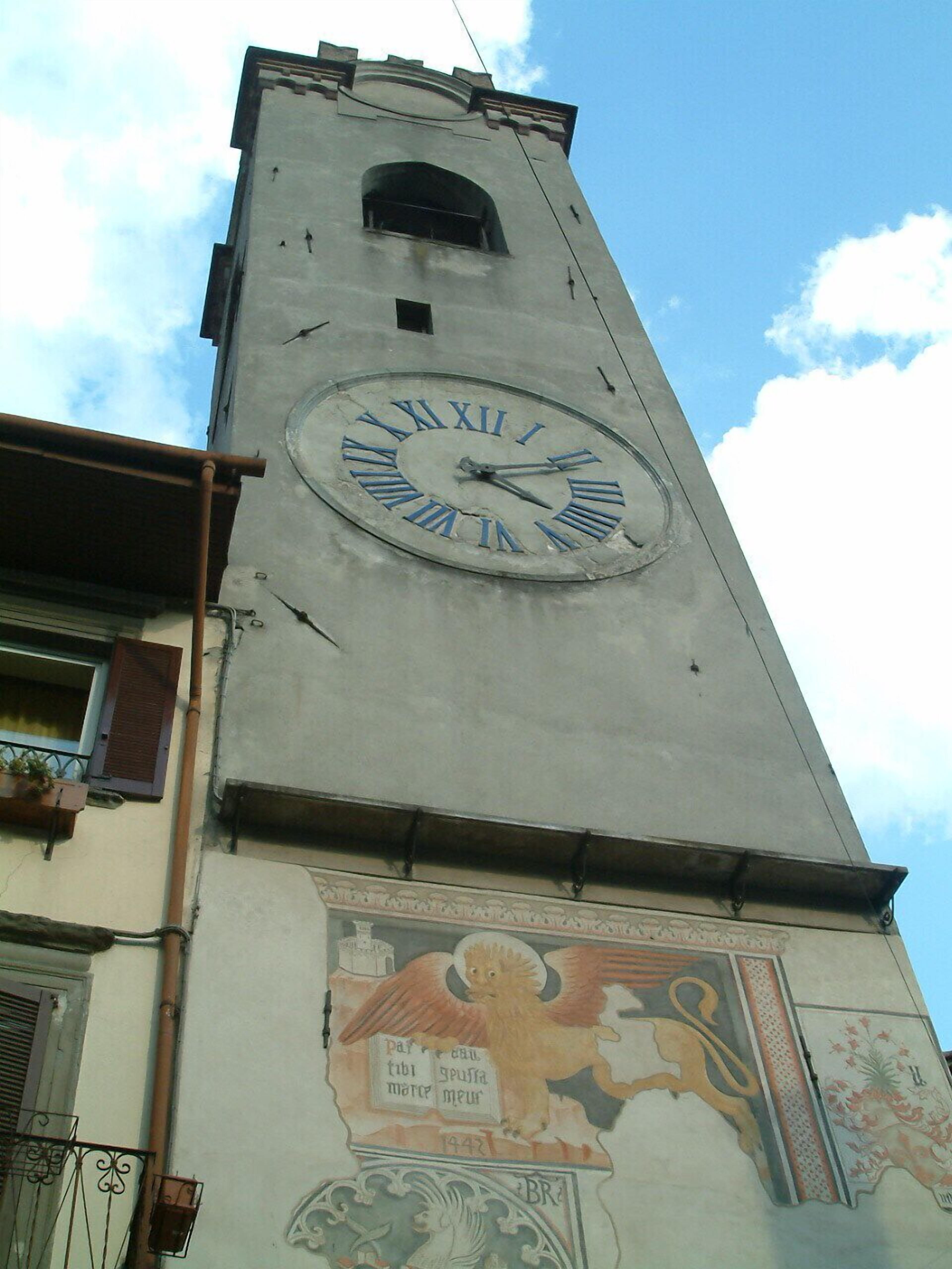 Une tour de l’horloge surmontée d’une grande horloge et ornée d’une fresque murale en dessous.