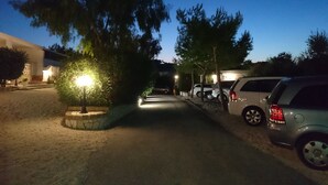 Un área de estacionamiento nocturno con árboles y un camino que lleva a un edificio.
