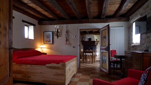 A wooden bed with a red blanket, a red sofa, a wooden dresser, and a dining area with a table and chairs. - The Music Country House, between Asolo, the Prosecco hills and Monte Grappa (Castelcies)