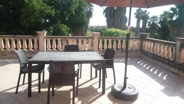 An outdoor patio with a table and chairs, a large umbrella, and a balustrade. - Korisia accommodation in villa delle canfore surrounded by an olive grove with sea view (AVOLA)