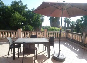 Un patio al aire libre con mesa y sillas, un parasol grande y una barandilla.