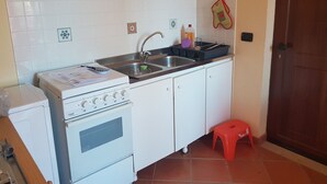 A compact kitchen with a stove, sink, and a small stool. - Korisia accommodation in villa delle canfore surrounded by an olive grove with sea view (AVOLA)