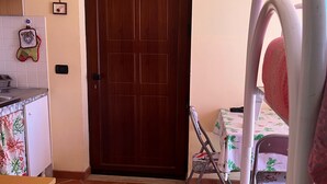 A room with a wooden door, tiled floor, a small table with a floral tablecloth, and a chair with a Union Jack design. - Korisia accommodation in villa delle canfore surrounded by an olive grove with sea view (AVOLA)
