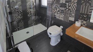 A modern bathroom with a glass-enclosed shower, a toilet, and a sink with a towel on the counter.