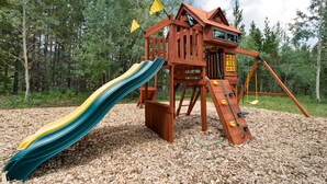 A wooden playground structure with a slide and climbing elements, surrounded by trees and a clear sky. - Copper Moose on Main Street Awaits You!! (Breckenridge)