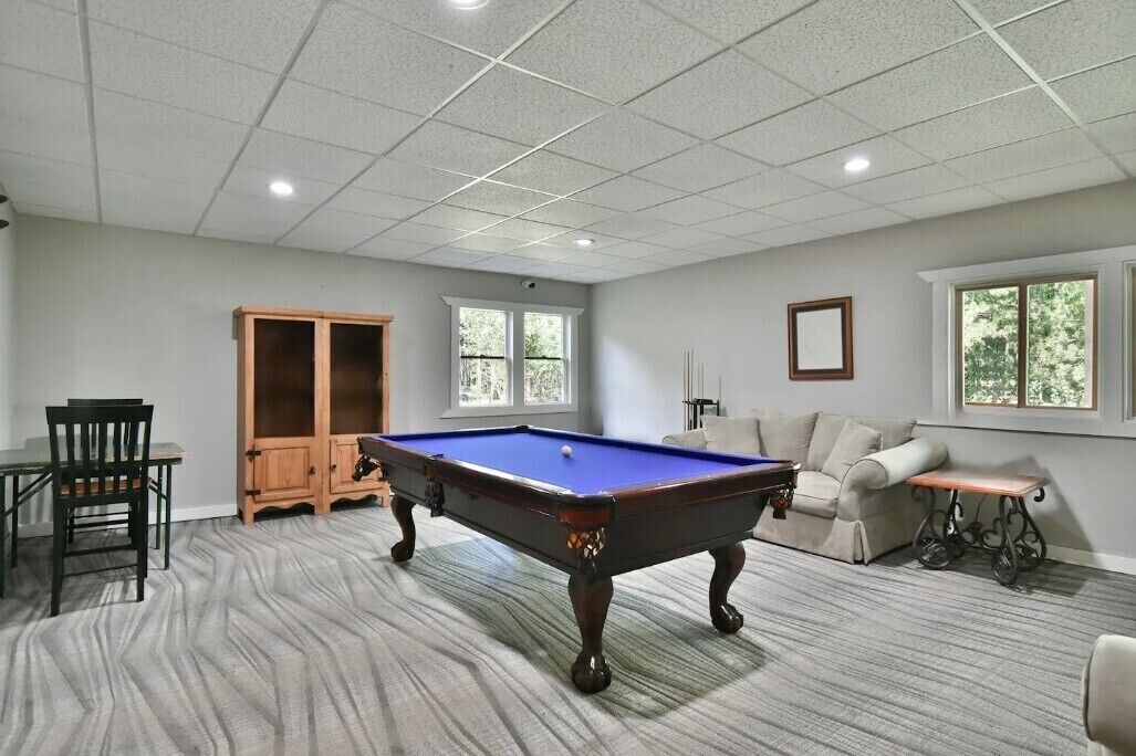 Una habitación con mesa de billar, un sofá, una silla, un armario de madera y una ventana.