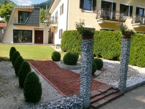 Uma casa moderna de dois andares com um jardim bem cuidado, incluindo sebes podadas e um caminho de cascalho.