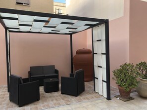 A covered outdoor seating area with a table and chairs, a large terracotta pot, and a potted plant. - Shardan Guest House (Alghero)