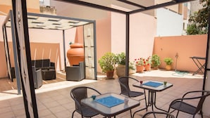An outdoor patio with tiled flooring, metal-framed chairs, and tables. There are potted plants and a large terracotta pot in the background. - Shardan Guest House (Alghero)