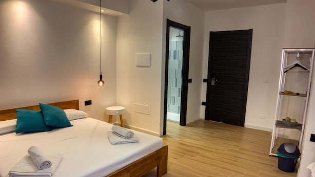 A hotel room with a wooden bed, white linens, teal pillows, a bedside table with a lamp, and a wardrobe with a mirror. - Shardan Guest House (Alghero)