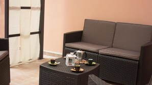 A cozy outdoor seating area with a cushioned sofa and a small table, both made of wicker. - Shardan Guest House (Alghero)
