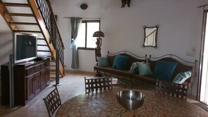 A living room with a wooden staircase, a sofa with cushions, a television on a cabinet, and a patterned floor. - BEAUTIFUL VILLA WITH SWIMMING POOL, RESIDENCE "SAFARI VILLAGE" WITH PRIVATE BEACH 100M (Unknown)