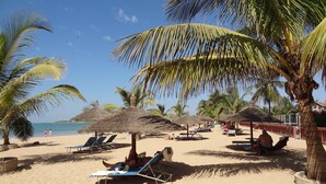 A beach with thatched umbrellas, lounge chairs, and palm trees. - BEAUTIFUL VILLA WITH SWIMMING POOL, RESIDENCE "SAFARI VILLAGE" WITH PRIVATE BEACH 100M (Unknown)
