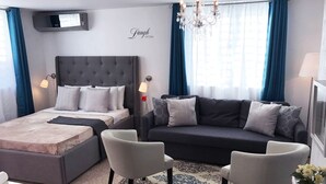 Una camera d'hotel moderna con un letto grande, un divano, due poltrone, un lampadario e una TV.