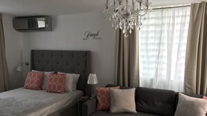 Una camera da letto con un letto, una poltrona, un lampadario, tende e un condizionatore d'aria a parete.